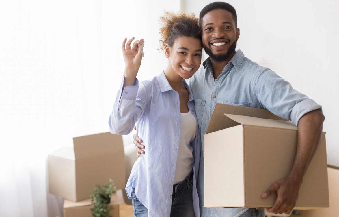 Couple Showing Key Holding Moving Box Standing In New Home